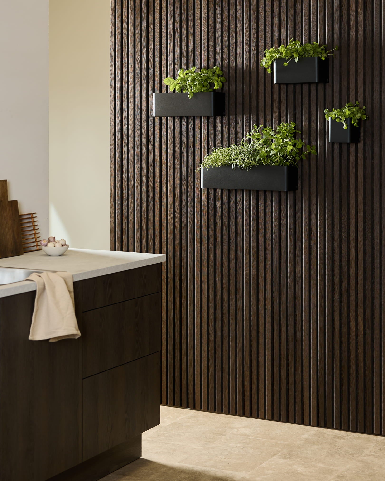 Moderne keuken met een WoodUpp Akupanel donkerhouten Akoestisch paneel, black Norr Plant Box met kruiden, en donkere kasten met een wit werkblad.